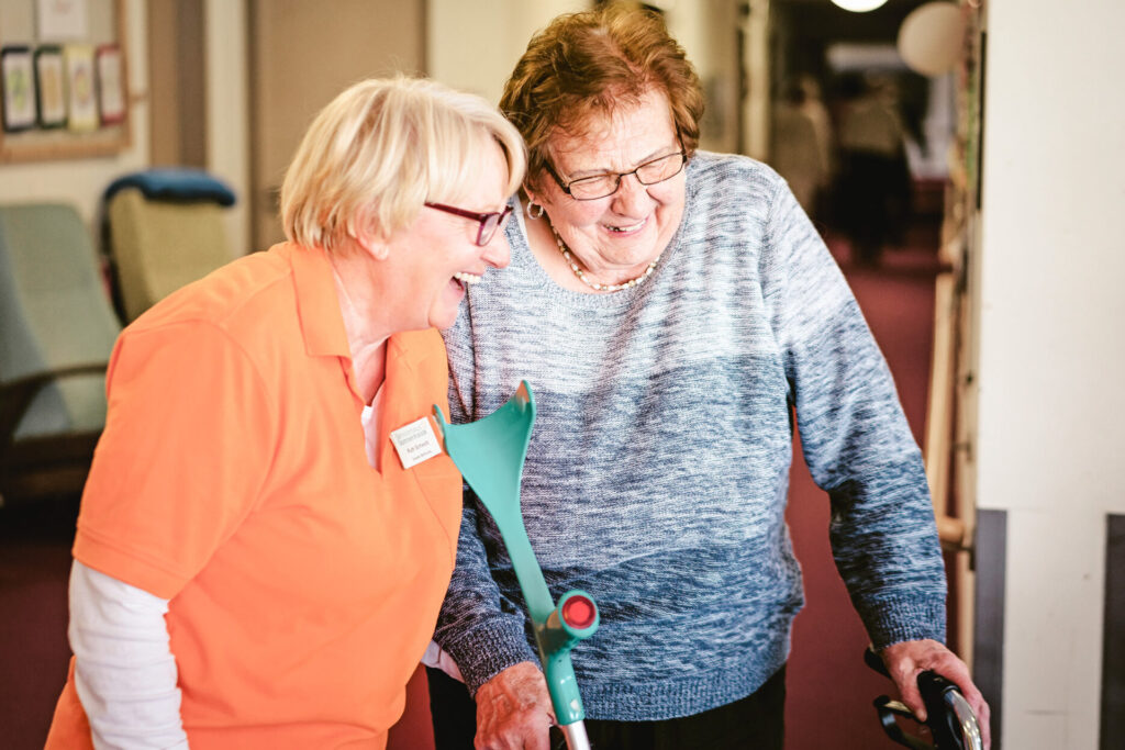 Herzliche Betreuung: Pflegekraft und Seniorin teilen einen fröhlichen Moment im Pflegeheim.