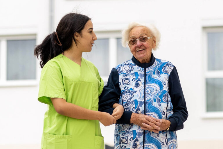 Liebevolle Betreuung: Pflegekraft unterstützt Seniorin beim Spaziergang in der Pflegeeinrichtung in Stetten